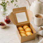 Box of french madeleines on a table with a teapot and coffee cup in the background