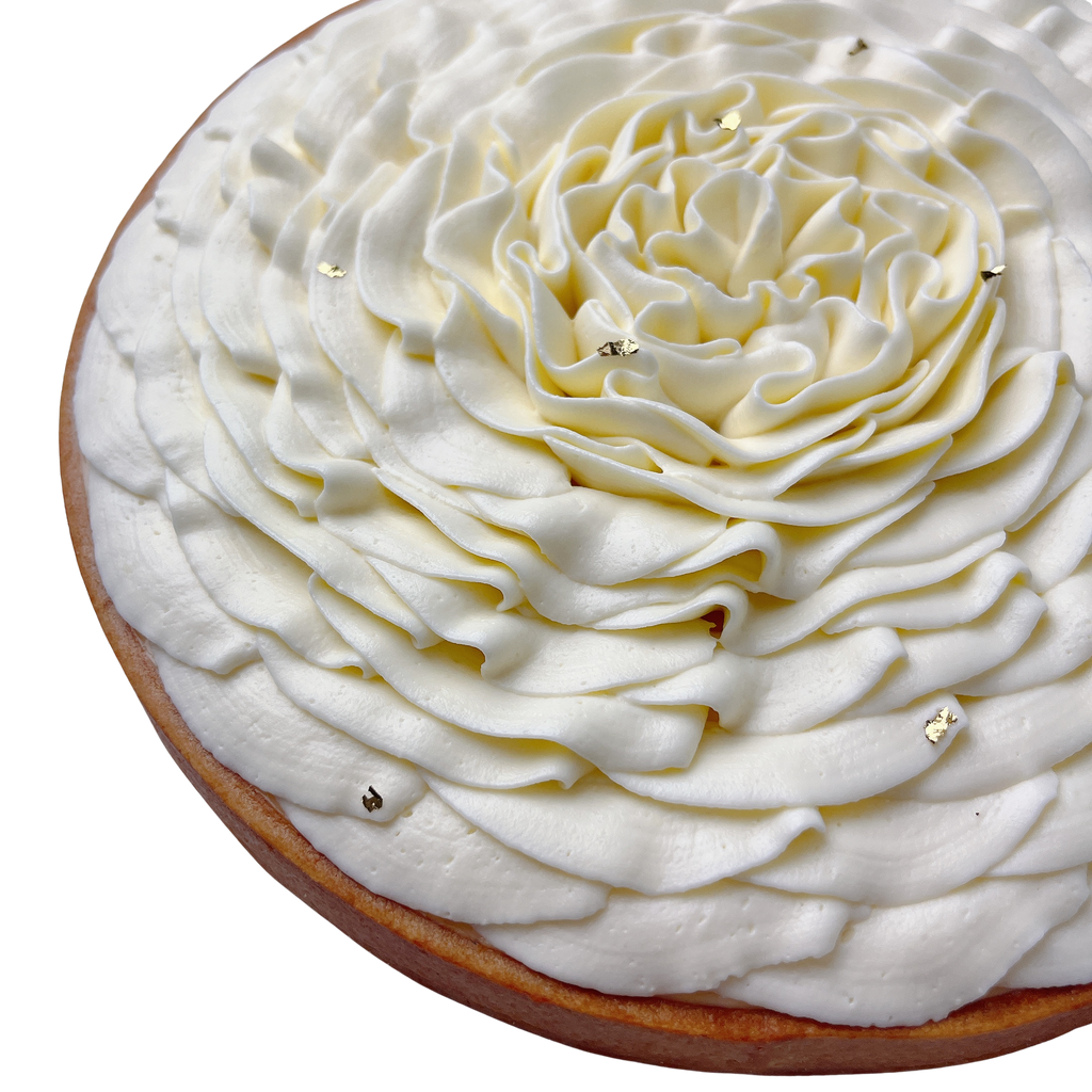 Angled close-up of a handcrafted French lemon tart topped with vanilla whipped cream flower and edible gold leaf.